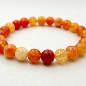 May include: A bracelet with round, faceted beads in orange, yellow, and red hues. The natural stone beads are strung on elastic. Each bead is approximately 0.8 cm in diameter. A vibrant piece of jewellery.