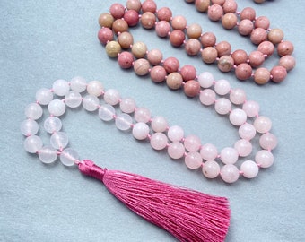 Puede incluir: Un collar mala de piedras preciosas rosa y blanco con un borla rosa. El collar está hecho de cuentas redondas y tiene aproximadamente 108 cuentas.