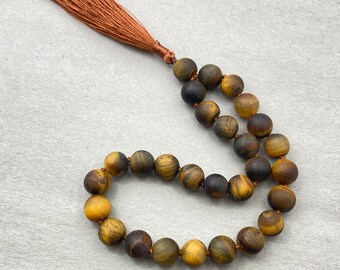 May include: A brown and gold tiger's eye beaded mala with a brown tassel.