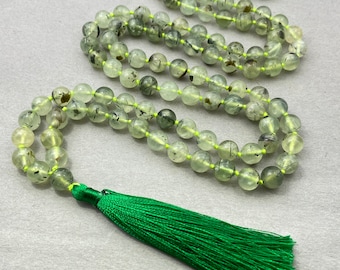 May include: A green mala necklace with a green tassel. The beads are made of green aventurine with black inclusions.