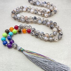 May include: A grey agate mala necklace with a grey tassel. The mala features seven chakra beads in rainbow colours.