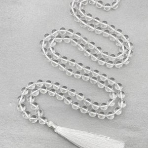 Puede incluir: Un collar mala de cristal transparente con un borla blanca. El collar est&aacute; hecho de cuentas redondas y tiene aproximadamente 108 cuentas.