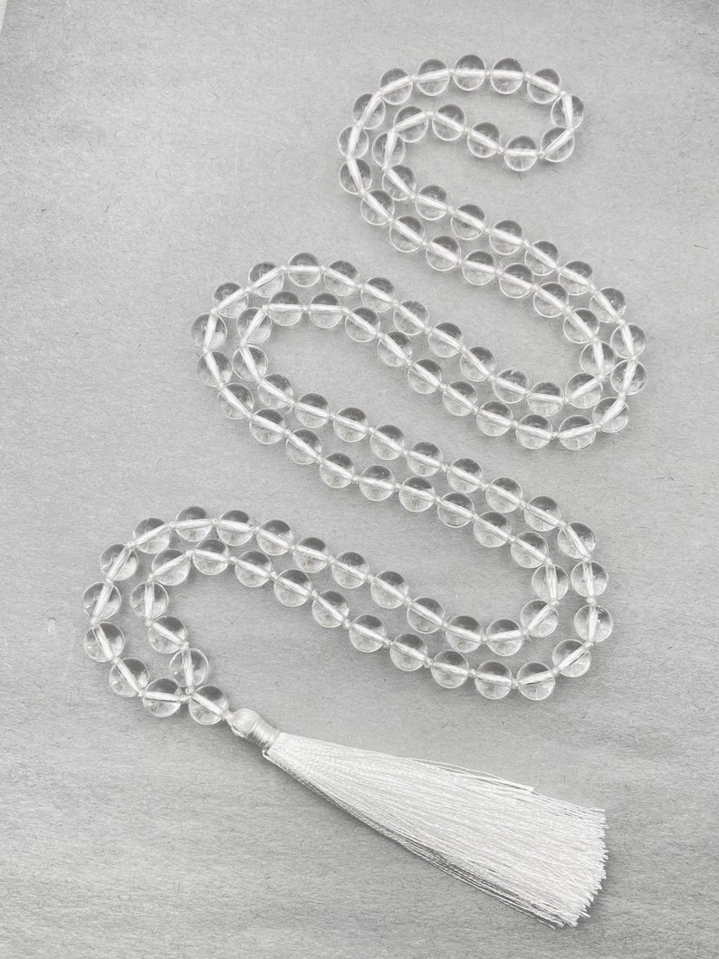 Puede incluir: Un collar mala de cristal transparente con un borla blanca. El collar est&aacute; hecho de cuentas redondas y tiene aproximadamente 108 cuentas.