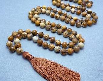 May include: A brown and white jasper stone mala necklace with a brown tassel. The necklace is made of 108 beads and is approximately 18 inches long.