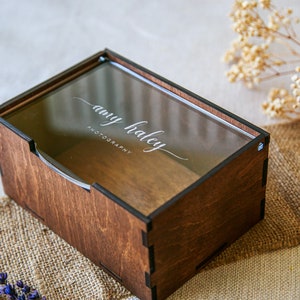 May include: A rectangular dark brown wooden box with a clear acrylic sliding lid. The lid features the white printed text "amy haley PHOTOGRAPHY" in a combination of script and sans-serif fonts. The box has visible interlocking corner joints.