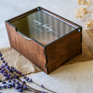 May include: A rectangular wooden box with a dark brown finish and a clear acrylic lid. The lid features the white printed text "amy haley PHOTOGRAPHY" in a script and sans-serif font. The box has visible interlocking joints at the corners.