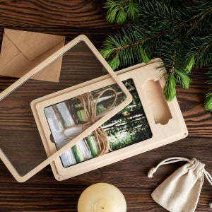 May include: A wooden box with a clear acrylic lid, containing a photograph of a forest scene with a brown ribbon tied around it. The box is sitting on a wooden surface.