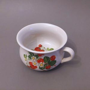 May include: White ceramic mug with a handle, featuring a floral pattern of red strawberries and white flowers.