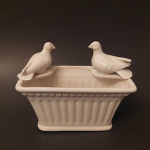 以下が含まれることがあります： 白い陶器製のプランターに、白い陶器製の鳩が2羽、縁に止まっている。プランターは長方形で、縦の筋が入っており、縁はギザギザになっている。