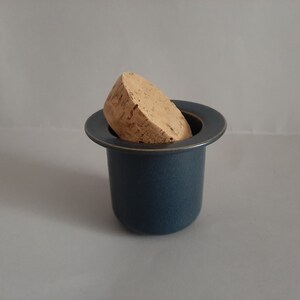 May include: A dark blue ceramic jar with a cork lid. The jar has a wide, flat rim and a slightly rounded body.