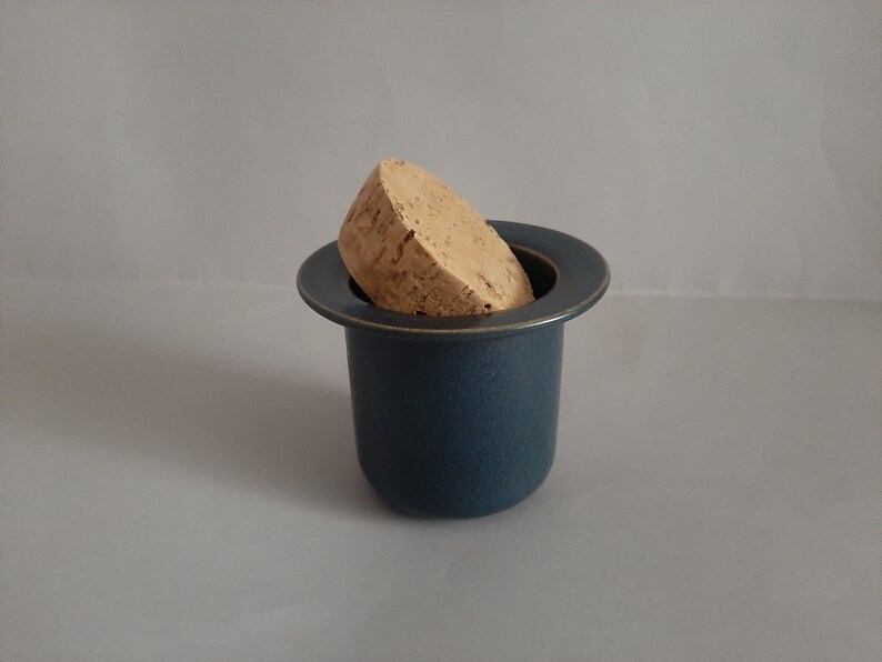 May include: A dark blue ceramic jar with a cork lid. The jar has a wide, flat rim and a slightly rounded body.