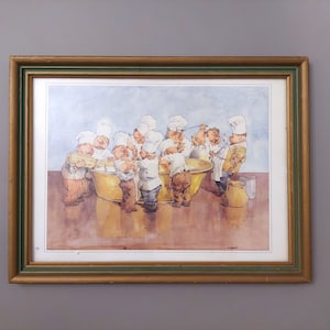 Puede incluir: Pintura a la acuarela enmarcada que representa a un grupo de chefs de dibujos animados con gorros y delantales blancos, reunidos alrededor de un gran cuenco dorado. La obra de arte está enmarcada en un marco de madera dorado y verde.