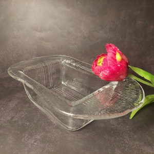 Op de afbeelding: Een rechthoekige glazen schaal van helder glas met een getextureerd oppervlak. Een enkele rode tulp met gele accenten rust op de rand van de schaal.