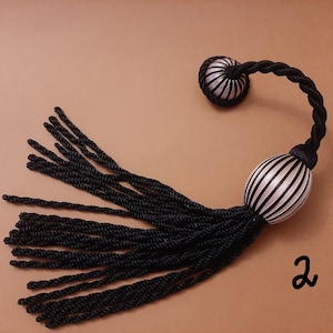 Puede incluir: Borla a rayas blancas y negras con un cordón negro y dos bolas redondas de tela a rayas. La borla mide aproximadamente 45 cm de largo.