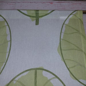 May include: Two white and green leaf-patterned curtains. The design features large, stylized green leaves with detailed vein patterns against a white background. The curtains are hanging from a gold-colored rod, adding a touch of elegance.