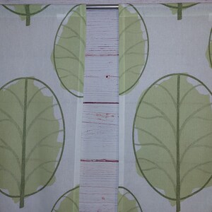 May include: Two white curtain panels with a repeating pattern of large, stylized green leaves. The leaves have a dark green outline and a lighter green fill. The curtains are hanging on a silver rod.