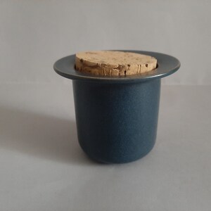 May include: A dark blue ceramic jar with a cork lid. The jar has a wide rim and a smooth, textured surface.