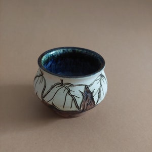 May include: A small, white ceramic bowl with a blue glaze inside and a brown and white leaf design on the outside.