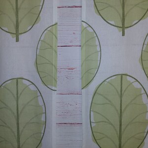 May include: White fabric with a repeating pattern of large, stylized green leaves. The leaves have a simple outline and a filled-in, textured appearance. The design is symmetrical and creates a natural, botanical theme.