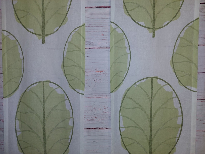 May include: White fabric with a repeating pattern of large, stylized green leaves. The leaves have a simple outline and a filled-in, textured appearance. The design is symmetrical and creates a natural, botanical theme.