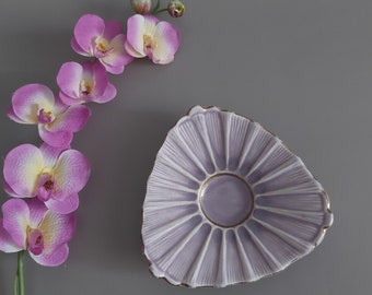 Peut inclure: Un plat décoratif en céramique violet clair avec un bord doré et un motif en éventail. Le plat est placé à côté d'une tige d'orchidées roses et jaunes sur un fond gris.