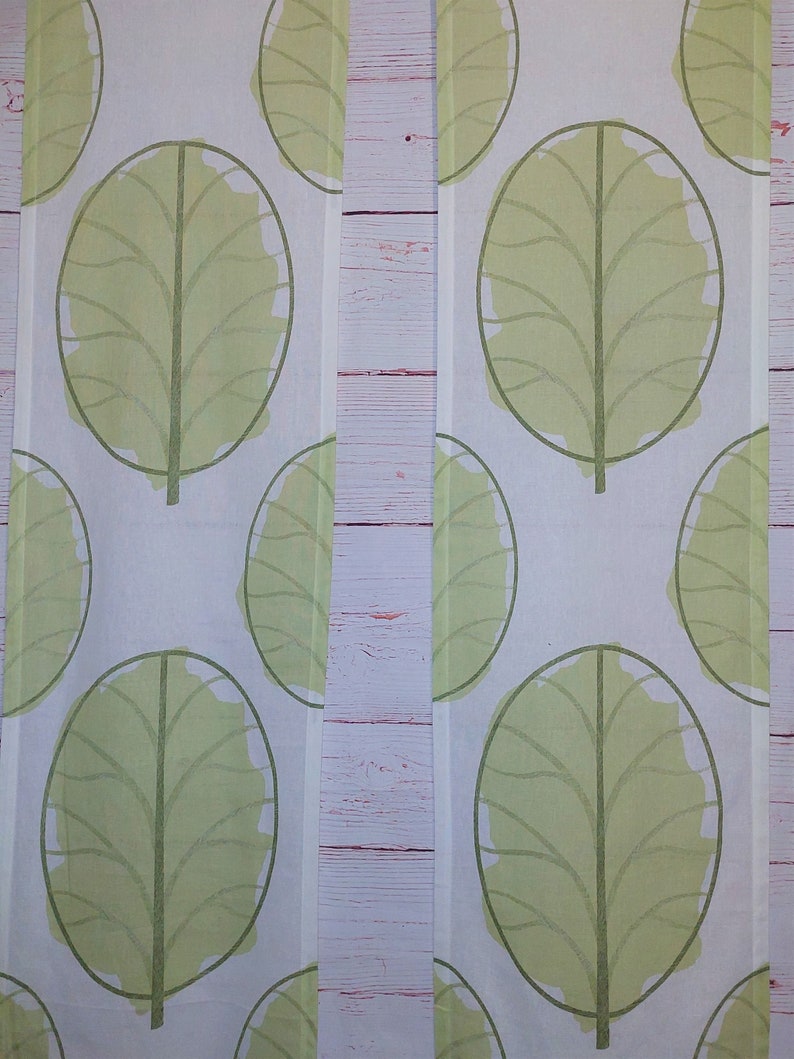 May include: Two white fabric panels with a repeating pattern of large, light green leaf shapes. Each leaf has a dark green outline and a central vein. The background is a light, neutral color.