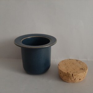 May include: A blue ceramic container with a cork lid. The container has a wide rim and a smooth, matte finish.