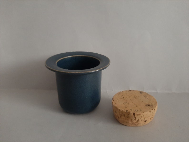May include: A blue ceramic container with a cork lid. The container has a wide rim and a smooth, matte finish.