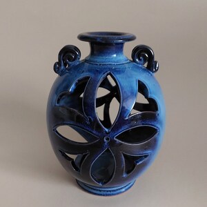 Könnte beinhalten: Eine blaue Keramikvase mit einem dekorativen Ausschnittmuster. Die Vase hat zwei Henkel und einen runden Körper.