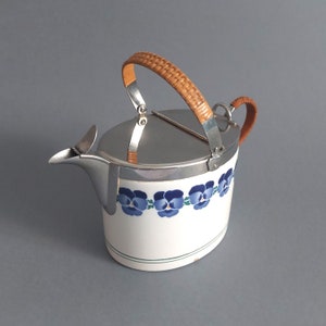 May include: White ceramic teapot with a silver lid and a woven brown handle. The teapot has a blue and green floral design.
