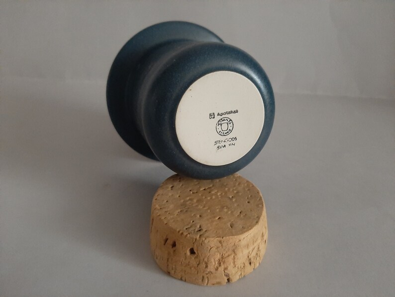 May include: A blue ceramic cup with a white bottom. The bottom has the text "Agapetus" and a logo with the text "STHLM-GDS" and "SWEDEN".