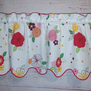 Peut inclure: Une cantonnière blanche avec un motif floral rouge, rose, jaune et marron. La cantonnière a un bord festonné et une bordure rouge.