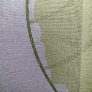 May include: Close-up of a sheer fabric with a floral design. The fabric features a white background with a green leaf pattern and a solid light green border. The fabric is likely used for curtains or home decor.