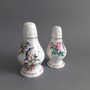 Op de afbeelding: Een paar witte porseleinen zout- en peperstrooiers met gouden rand. De strooiers hebben een bloemmotief met vogels en roze bloemen.