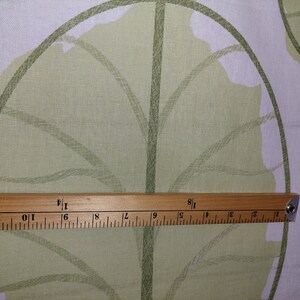 May include: Close-up of fabric with a large green leaf pattern on a white background. A wooden ruler shows measurements in inches. The fabric has a light green leaf design with darker green outlines.