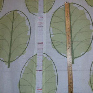 May include: Two panels of fabric with a repeating pattern of large, light green leaves on a white background. A wooden ruler is placed vertically, showing measurements up to 24 inches.