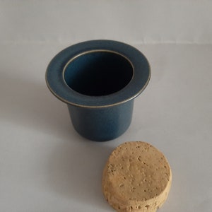 May include: A blue ceramic butter dish with a cork lid. The dish has a wide rim and a smooth, rounded shape.
