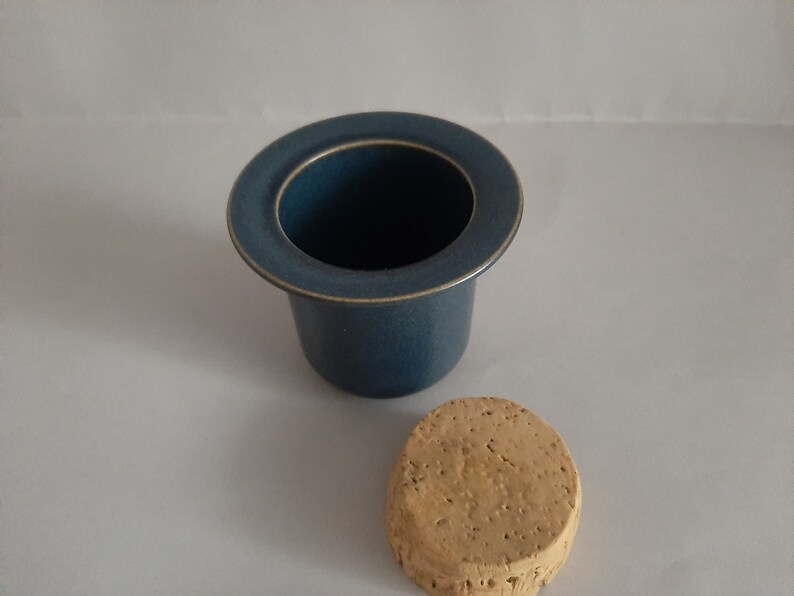 May include: A blue ceramic butter dish with a cork lid. The dish has a wide rim and a smooth, rounded shape.