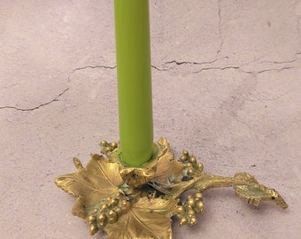 May include: A gold-toned metal candle holder shaped like a grapevine with a green candle. The candle holder has a detailed design with leaves and grapes.