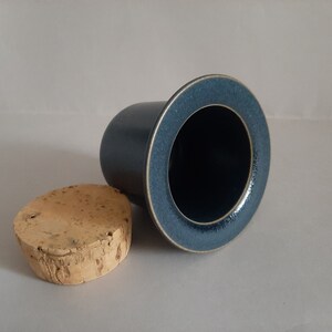 May include: A dark blue ceramic jar with a cork lid. The jar has a wide mouth and a smooth, slightly textured surface.