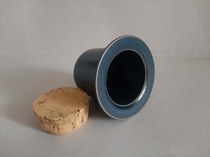 May include: A dark blue ceramic jar with a cork lid. The jar has a wide mouth and a smooth, slightly textured surface.