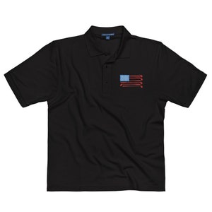 Puede incluir: Polo negro con un dise&ntilde;o de bandera estadounidense roja, blanca y azul hecho de palos de golf.