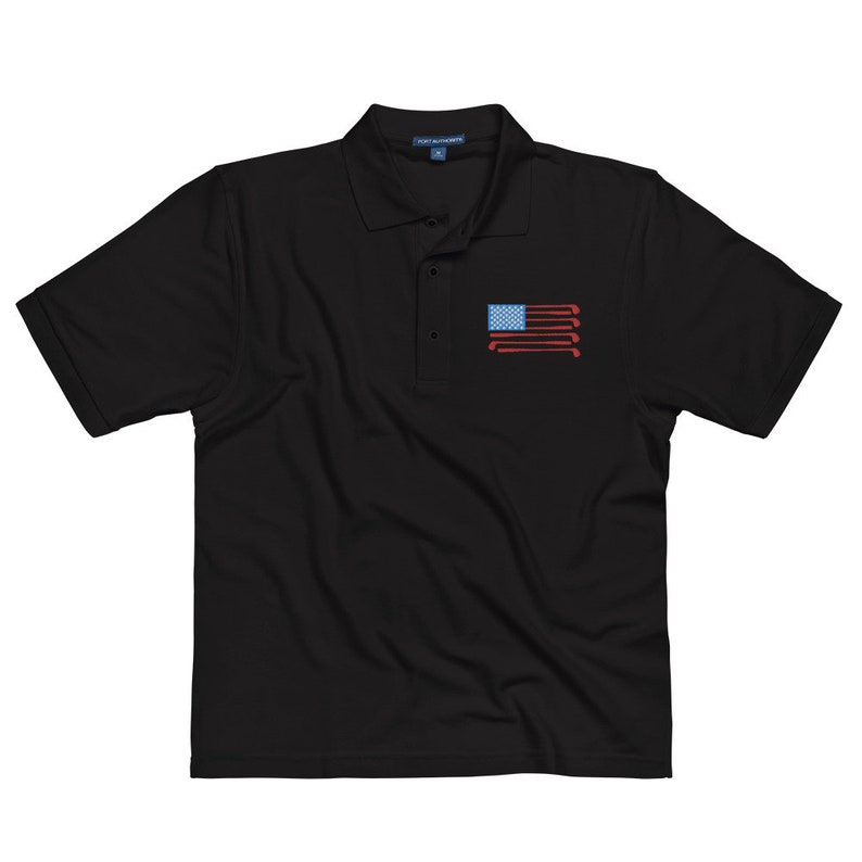 Puede incluir: Polo negro con un dise&ntilde;o de bandera estadounidense roja, blanca y azul hecho de palos de golf.