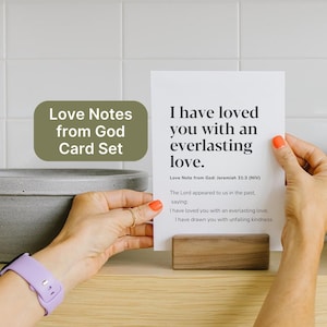 May include: A card set with the text "I have loved you with an everlasting love" is held in front of a white tile background. The card is propped up by a wooden block. The words "Love Notes from God Card Set" are in a green oval.