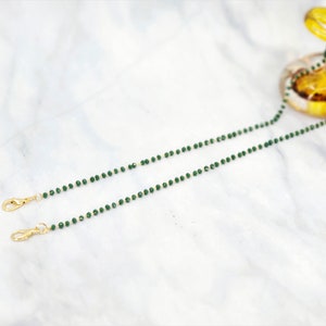 K&ouml;nnte beinhalten: Eine gr&uuml;ne Perlenkette mit goldenen Verschl&uuml;ssen. Die Kette besteht aus kleinen, runden Perlen und ist zum Tragen um den Hals gedacht.