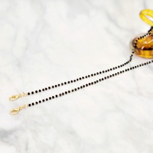 K&ouml;nnte beinhalten: Eine schwarze Perlenkette mit goldenen Verschl&uuml;ssen. Die Kette besteht aus kleinen, runden Perlen und ist etwa 60 cm lang.