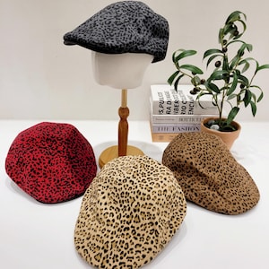 May include: Three different patterned newsboy caps. The caps are made of a soft, fuzzy fabric and feature a leopard print pattern in black, red, and brown.