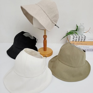 Peut inclure: Trois chapeaux bob de couleurs différentes : beige, blanc et vert. Les chapeaux ont une large bordure et un design simple.