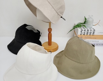 Może przedstawiać: Trzy kapelusze typu bucket w różnych kolorach: beżowym, białym i zielonym. Kapelusze mają szeroki rondel i prosty design.