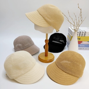 Puede incluir: Una colección de gorras de béisbol de malla en varios colores neutros, incluyendo beige, marrón claro y negro. Una gorra se muestra en una cabeza de maniquí. Las gorras tienen un diseño clásico con una visera curva y una textura tejida transpirable.
